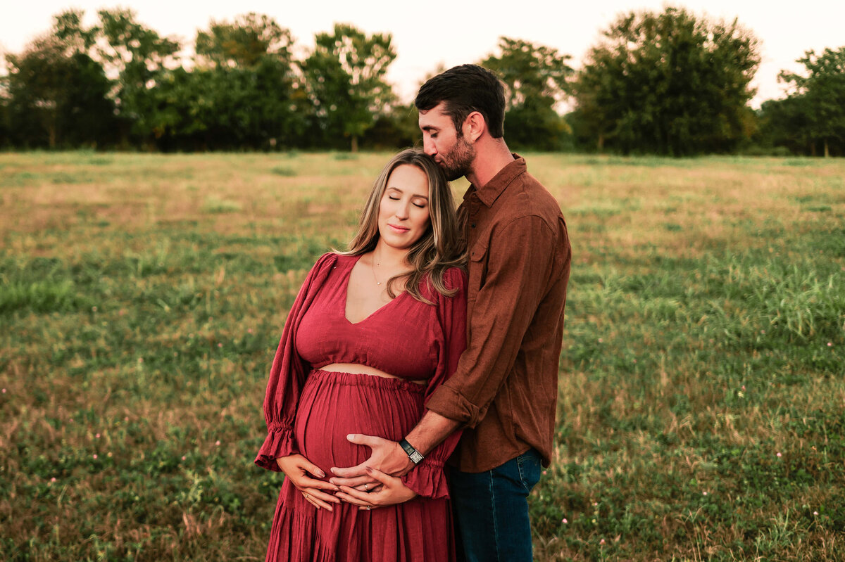 husband kissing pregnant moms head in field captured by Springfield MO maternity photographer Jessica Kennedy of The XO Photography