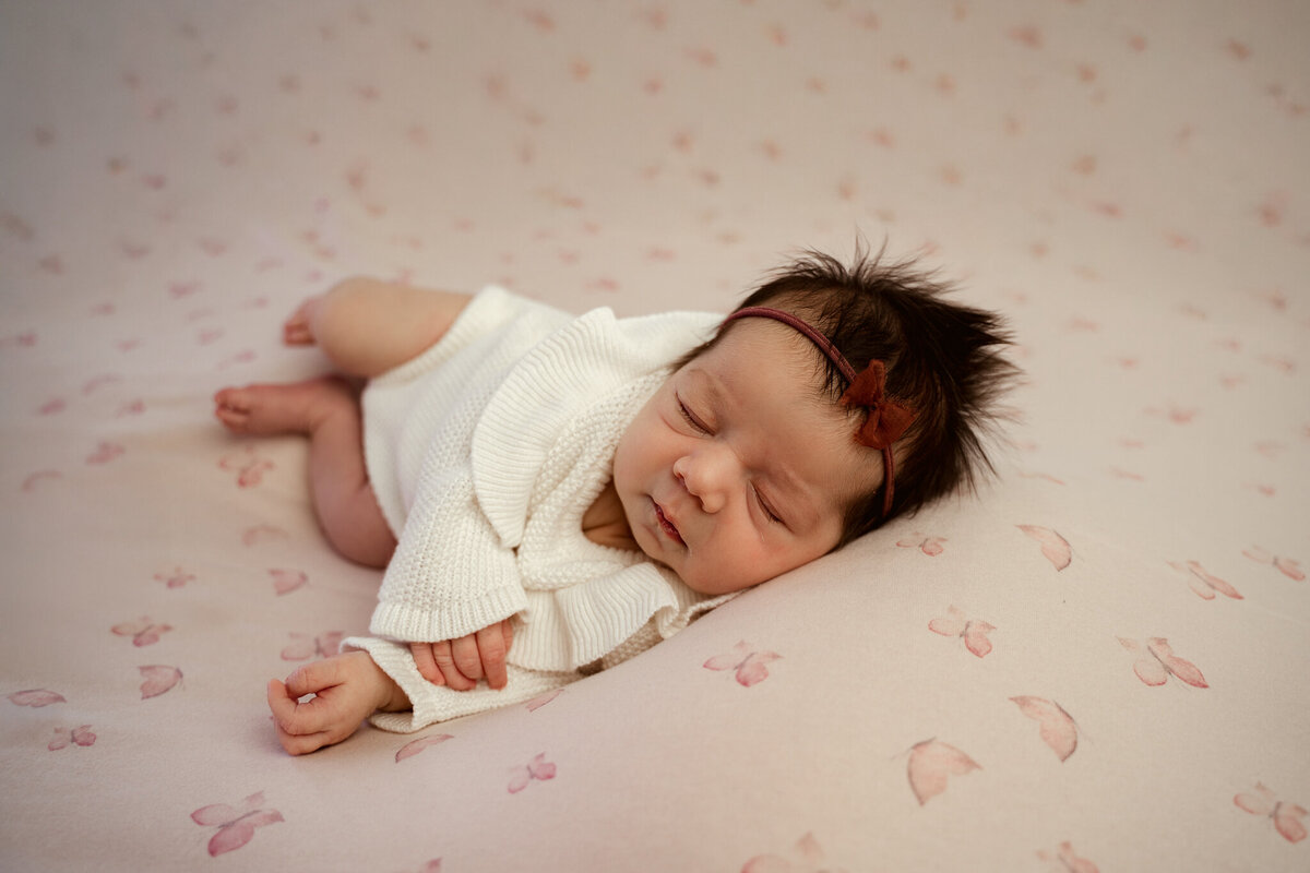 Side laying sleeping baby girl in knitted romper outfit; butterfly pink backdrop used; taken in Dothan, AL