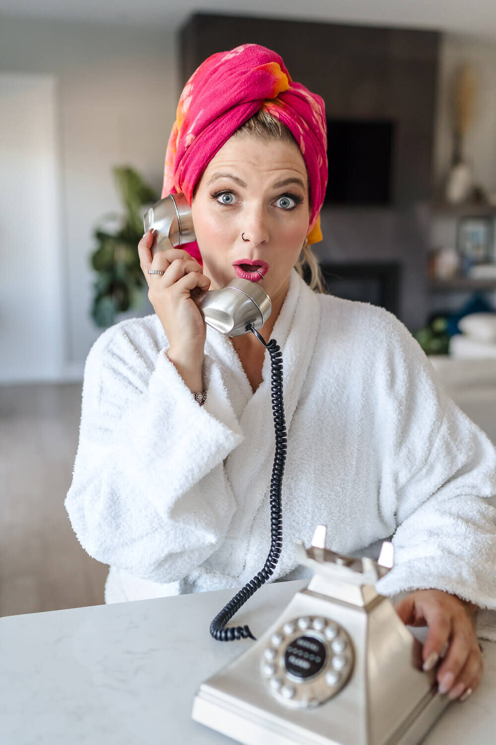 woman in pink towel turban and white bathrobe on silver retro phone with surprised expression