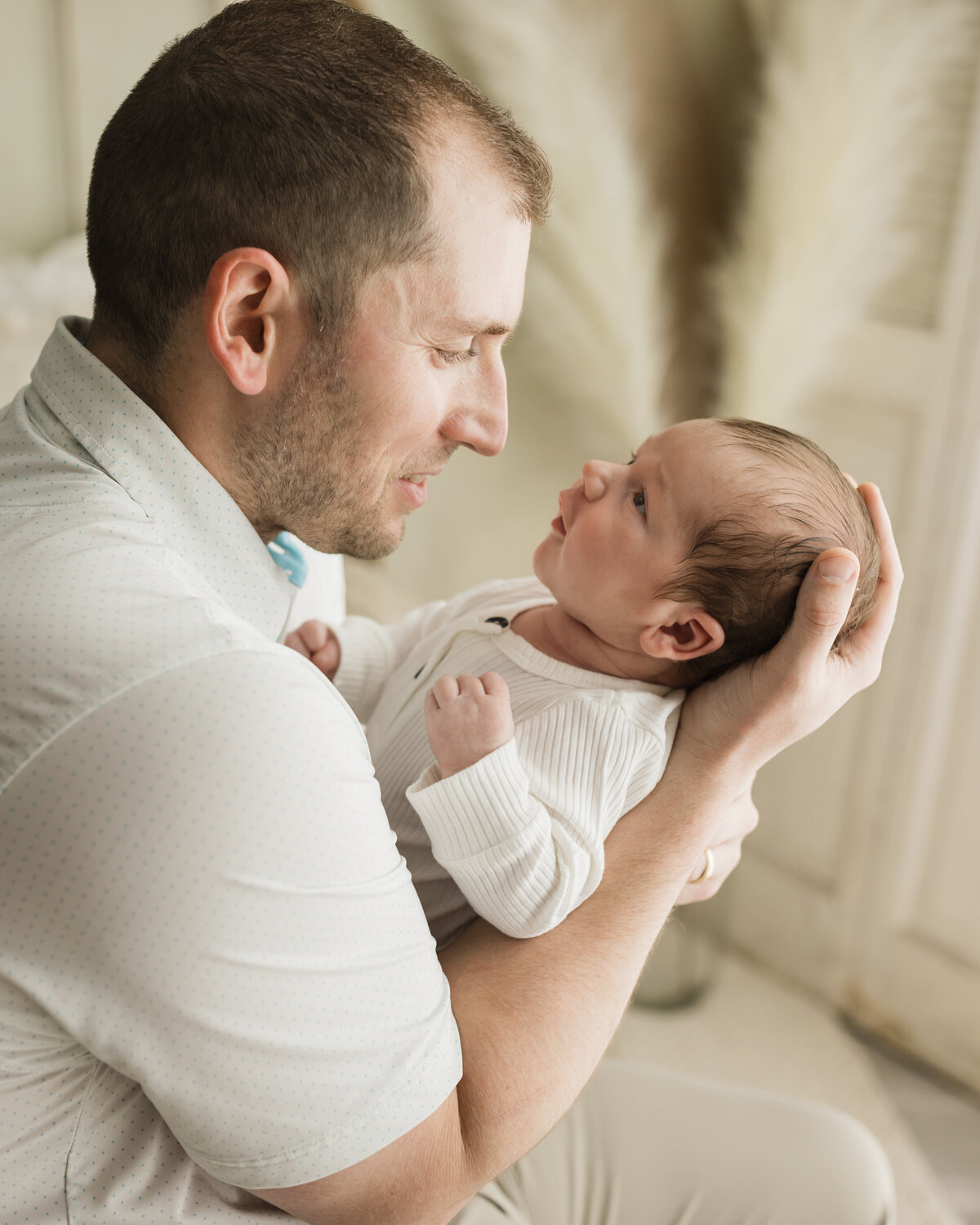 dad holding newborn baby boy in white onesie for studio photoshoot 