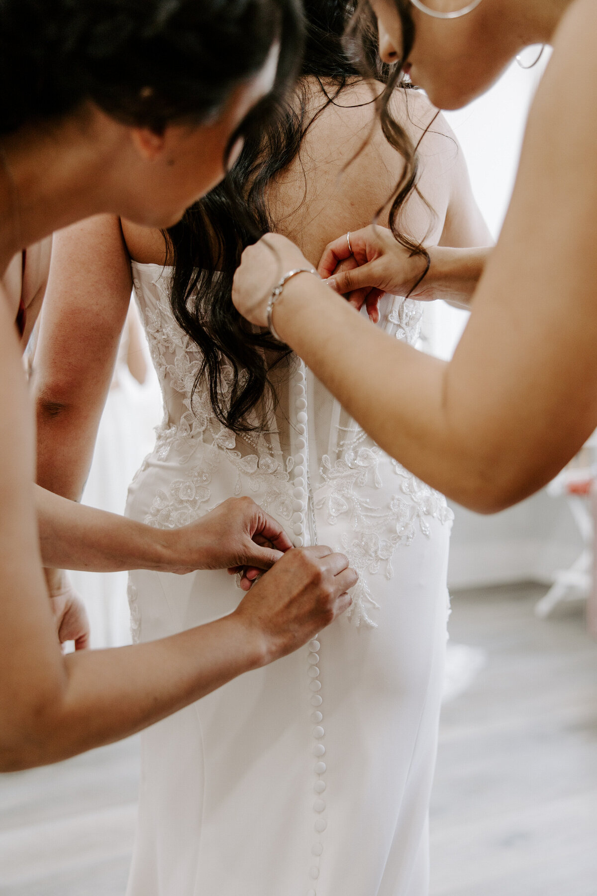 Friends help a bride button up her dress.