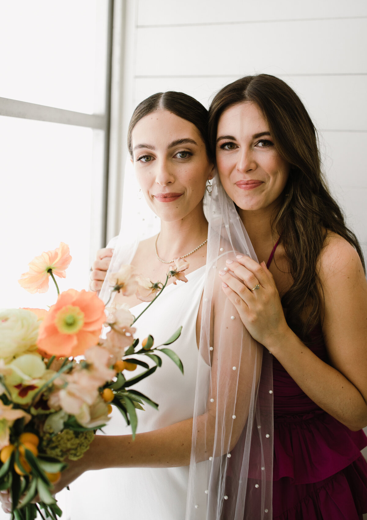Bride with wearing pearl veil and peach florals with woman in purple dress