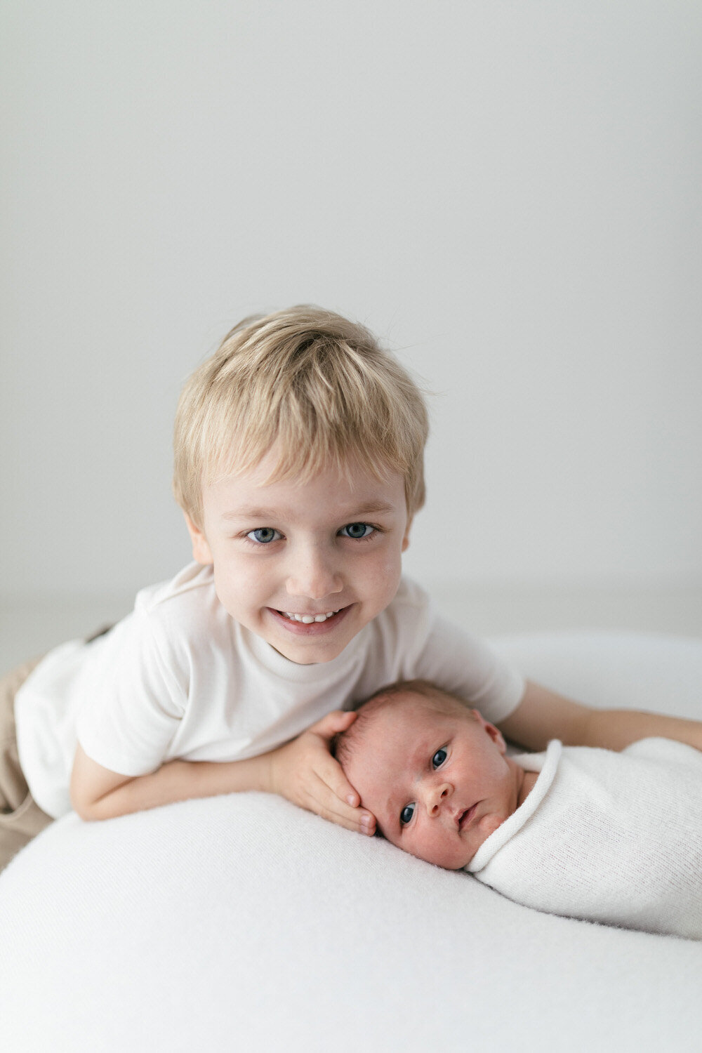 big brother holds newborn baby whilst smiling at the camera