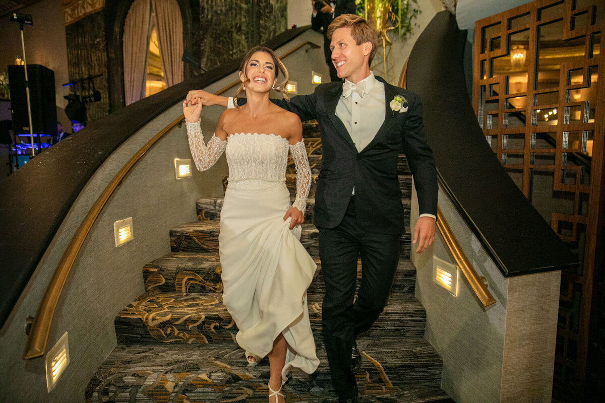A bride and groom are walking down a set of stairs