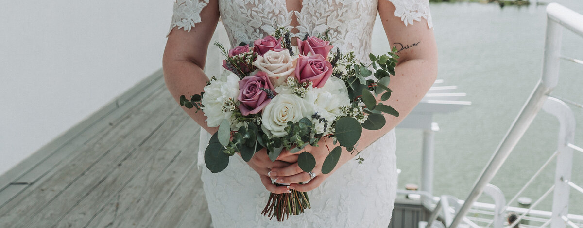 A close-up of a bride holding a beautiful wedding bouquet with pink, white, and green eucalyptus foliage, showcasing her off-the-shoulder lace gown at the Lesner Inn in Virginia Beach, captured by Quinn Photography LLC.