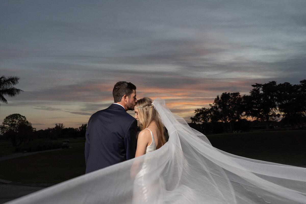Bride and groom embrace with a flowing veil against a Miami sunset backdrop.