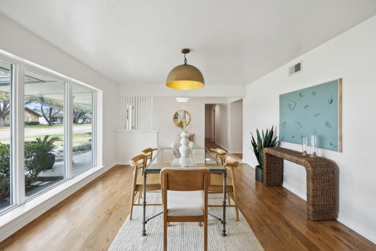 Dining room at 3120 Chapel Downs Dr Dallas TX featuring modern glass table, warm wood floors, statement lighting, and expansive front-facing windows — listed by Haven Realty Group.
