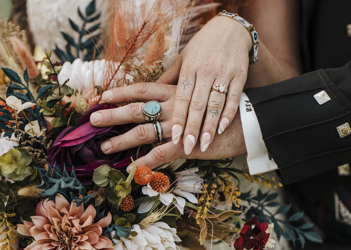United in matrimony: a couple's hands adorned with wedding bands, gently resting on a bouquet of delicate flora, symbolizing their love and commitment taken by jen Jarmuzek photography a Minneapolis wedding photographer