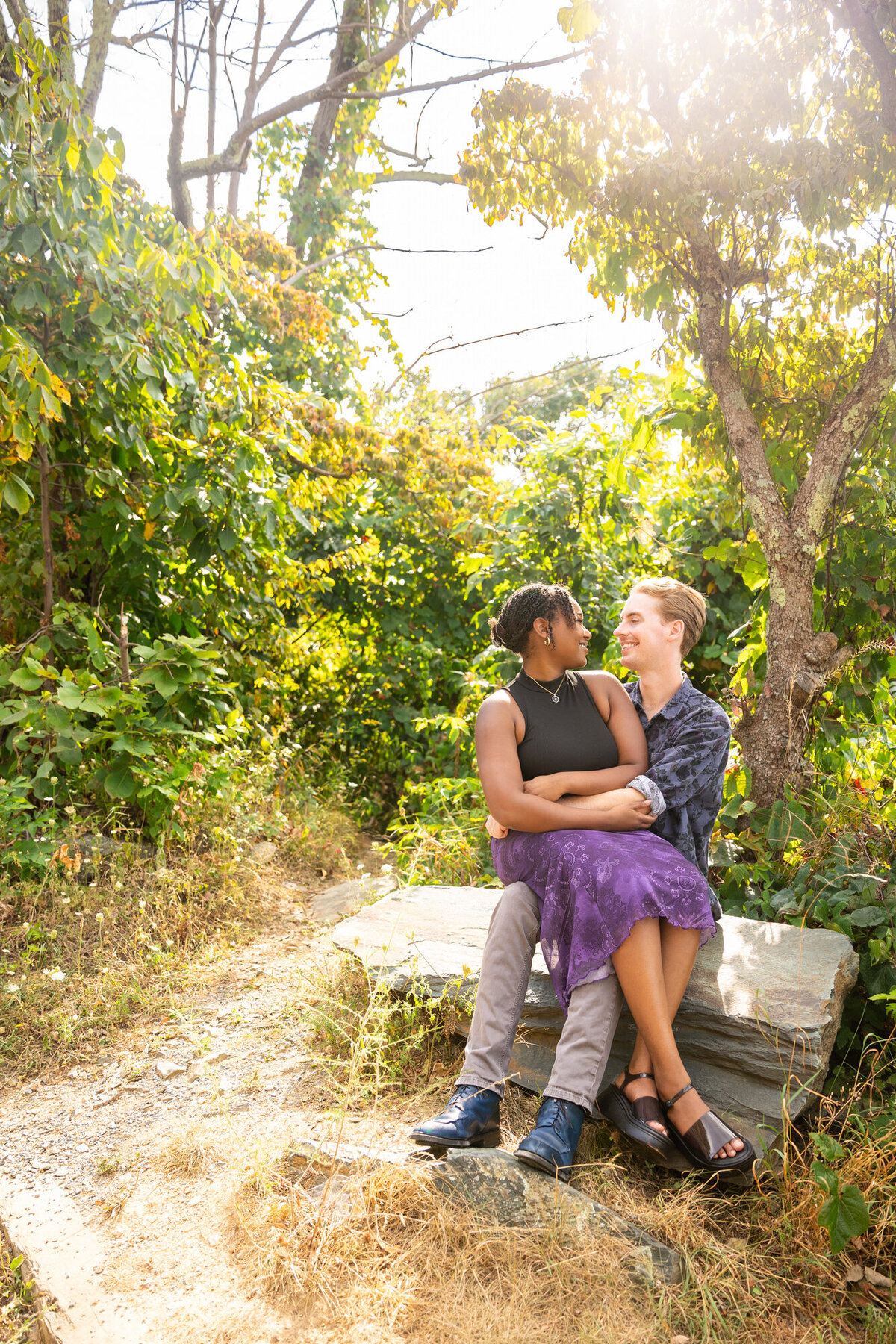 Shenandoah Engagement Couple looking at each other smiling while sitting on a rock during golden hour