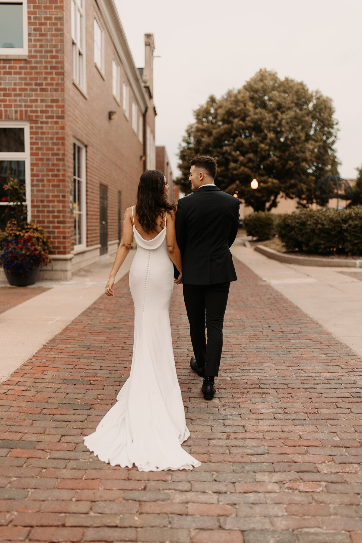 Bride and Groom walking away from the camera surrounded by brick buildings.