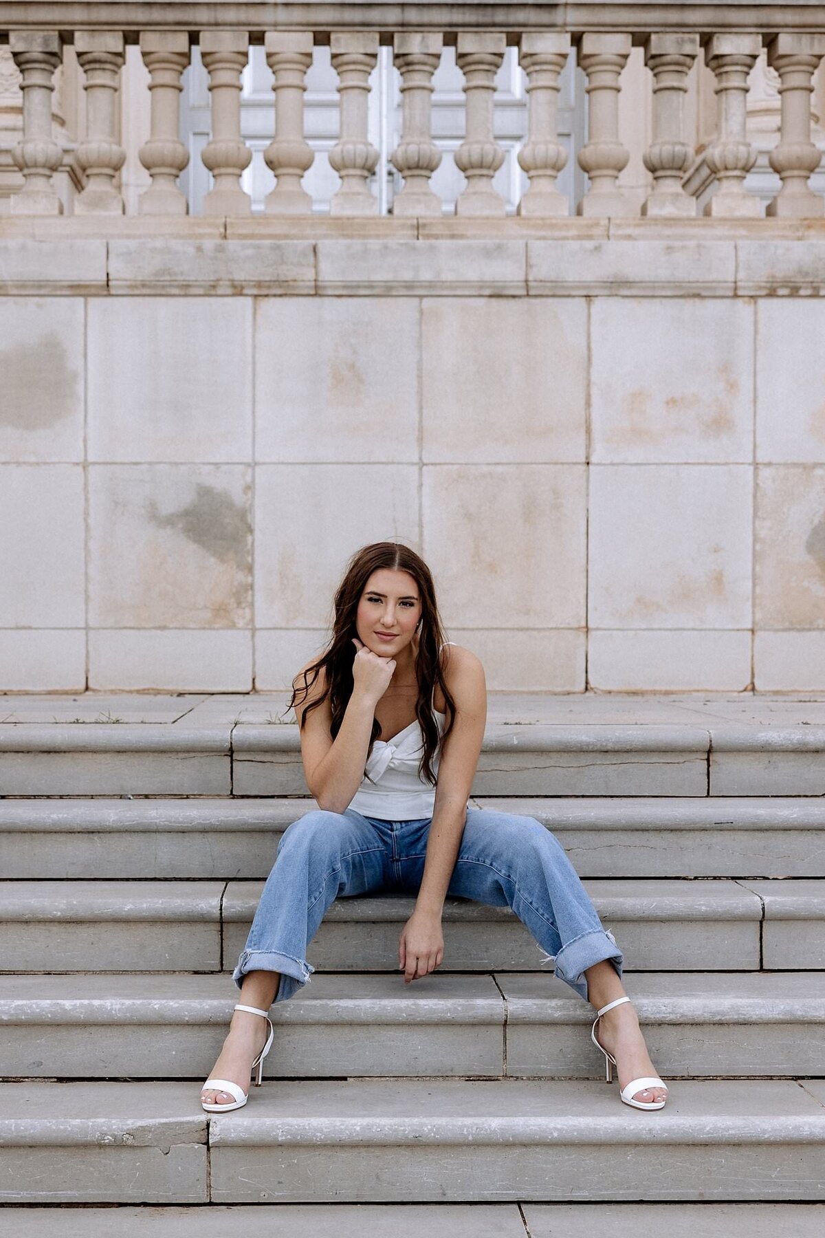 Lovely senior girl sitting on a concrete stairway with a stone wall behind her.