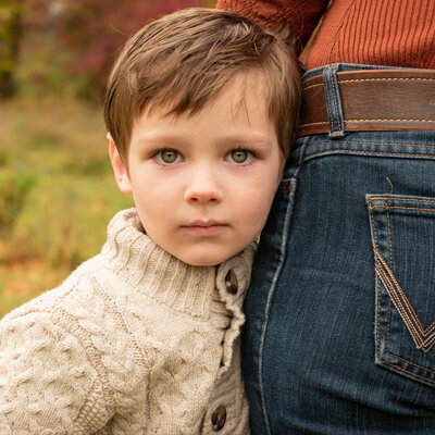 Young boy hugging mom's hip in fall.