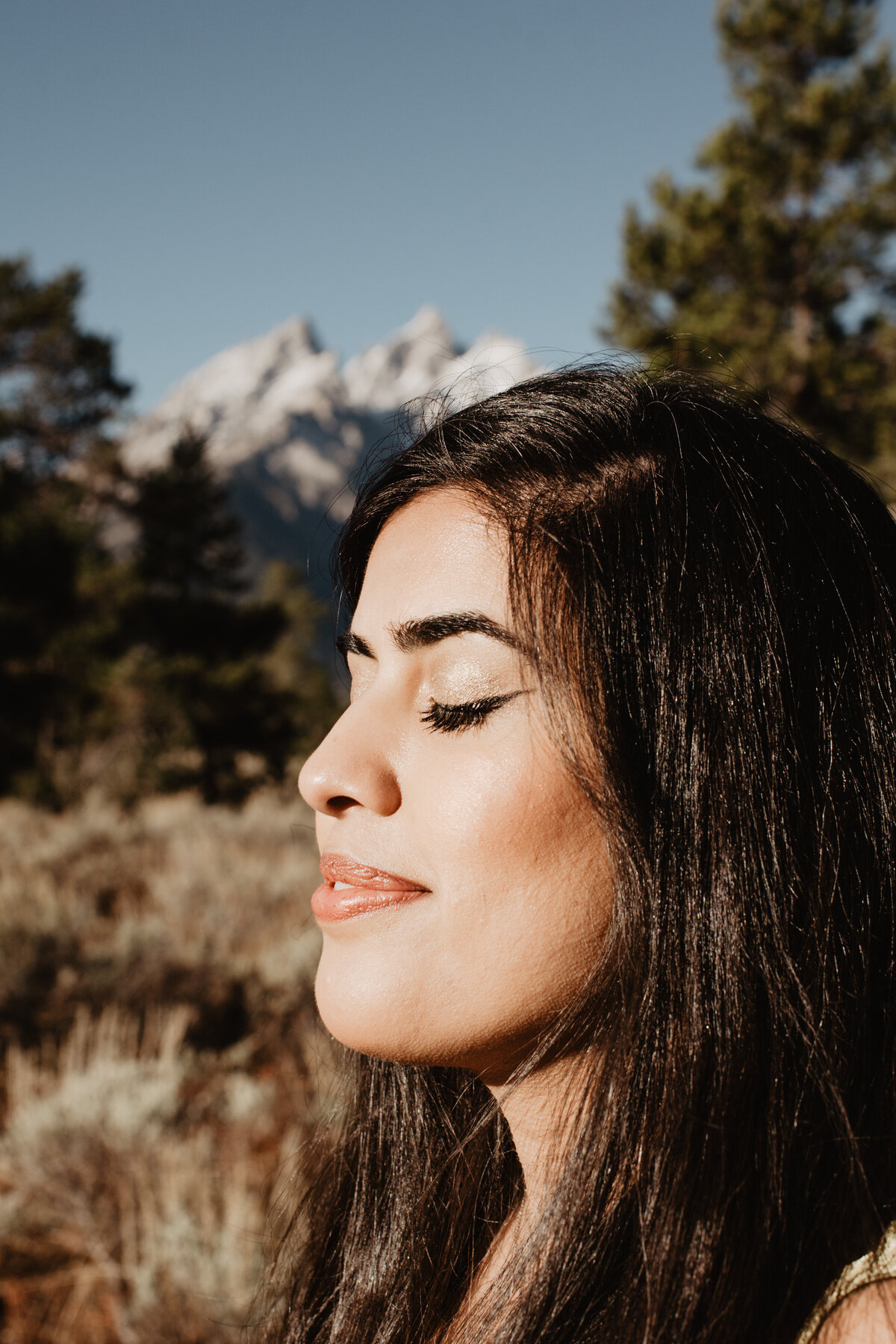 photographers in jackson hole captures jackson hole engagement pictures with woman smiling with her eyes closed and the sun on her face with the Tetons behind her