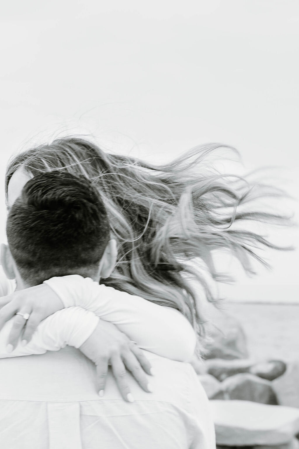 Rhode Island Wedding Photographers | A couple embraces at a beach, with their hair blowing in the wind. 