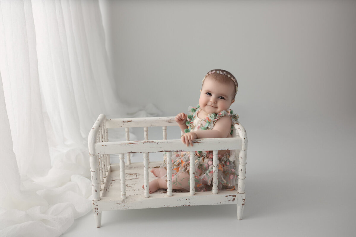 baby girl in dress sitting in crib photo by for the love of photography lansing
