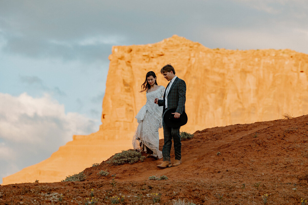A bridee and groom walking down a hill on their elopement day. The groom is helping the bride keep her balance while she holds her dress. 