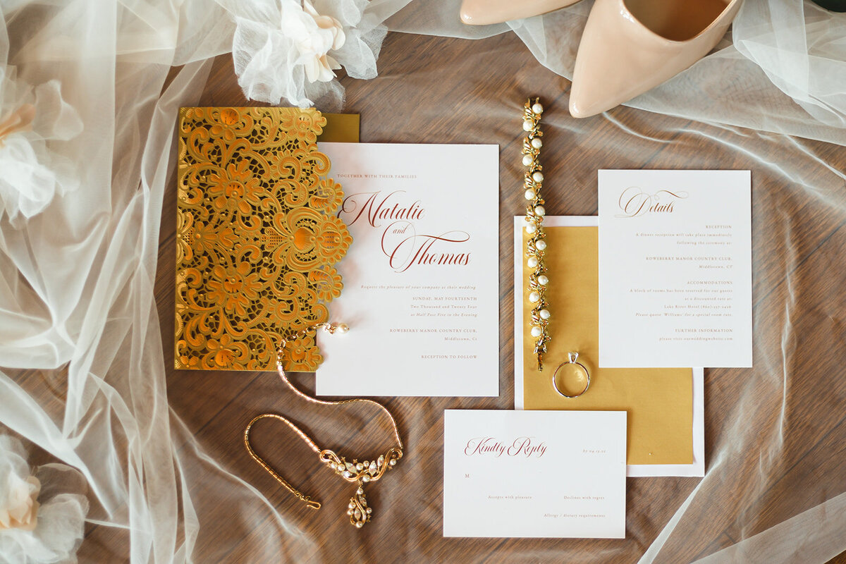 a flat lay of gold lace, white and gold invitations, and gold jewelry