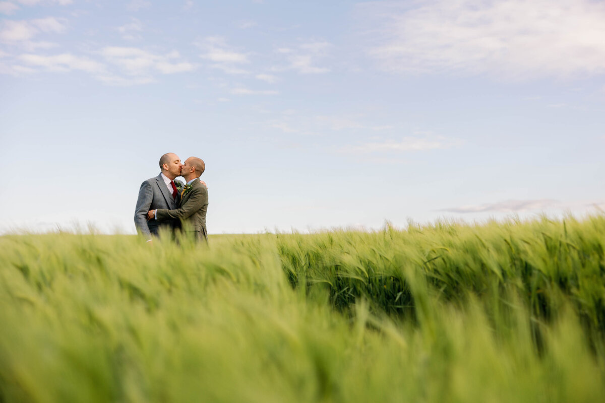 Gay male couple kissing in a field of long grass at Ellingham Hall
