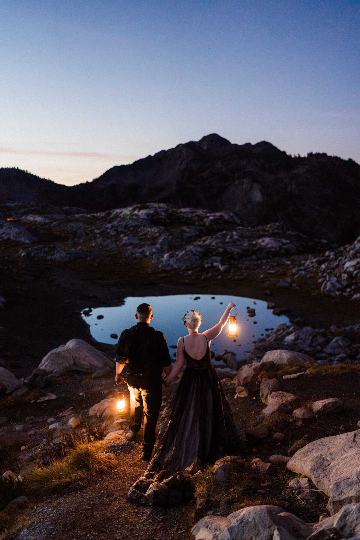 An adventurous hiking couple holding lanterns in front of mountain lake at sunset in the North Cascades