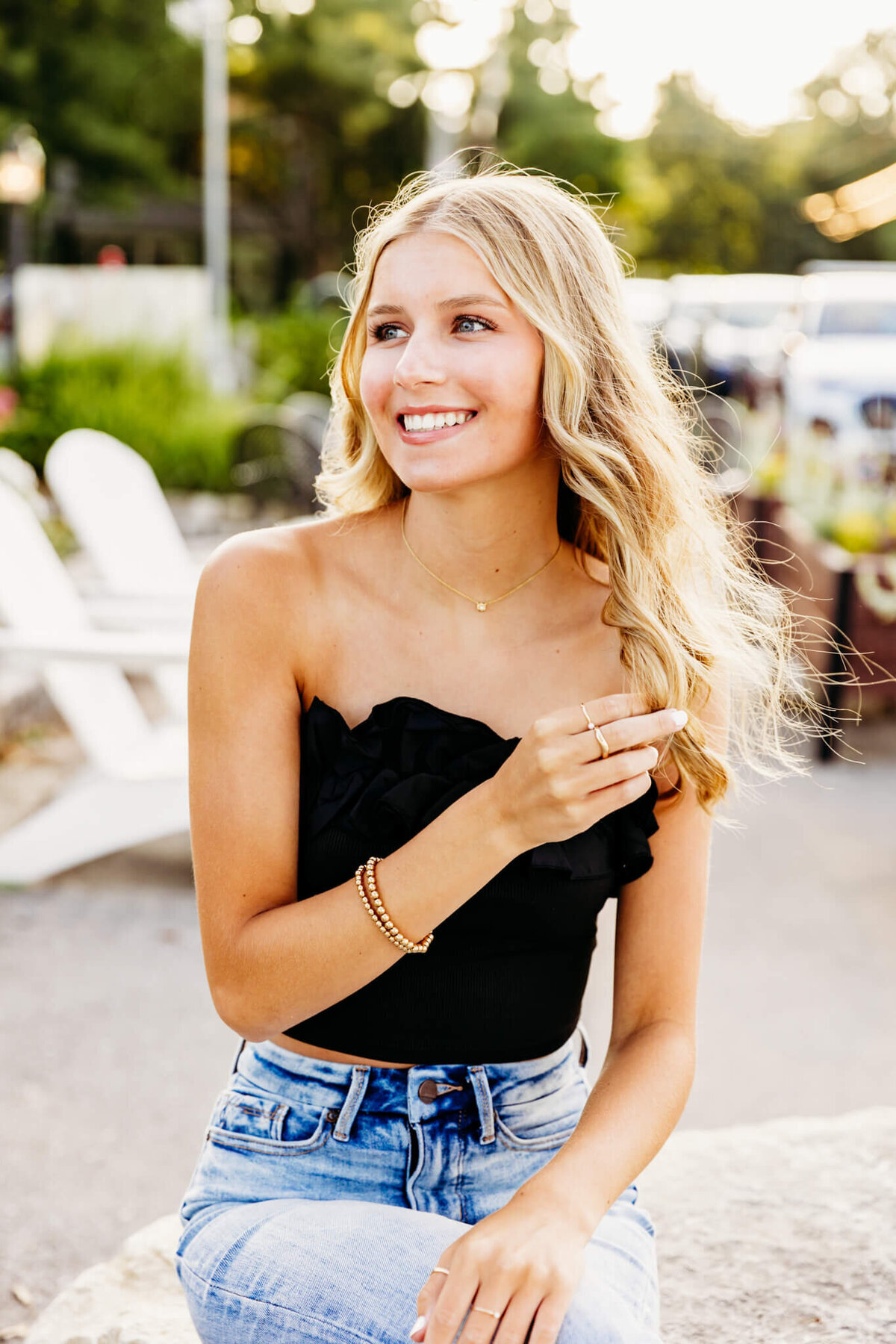 beautiful teen girl in a black top and jeans playing with her hair as she looks off to the side for her senior photography session