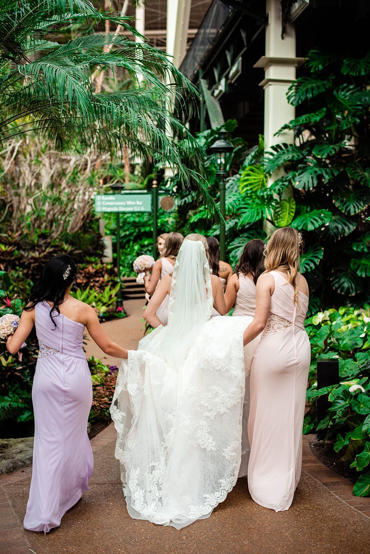Bride walking through Gaylord Opryland with her bridesmaids helping her carry her dress
