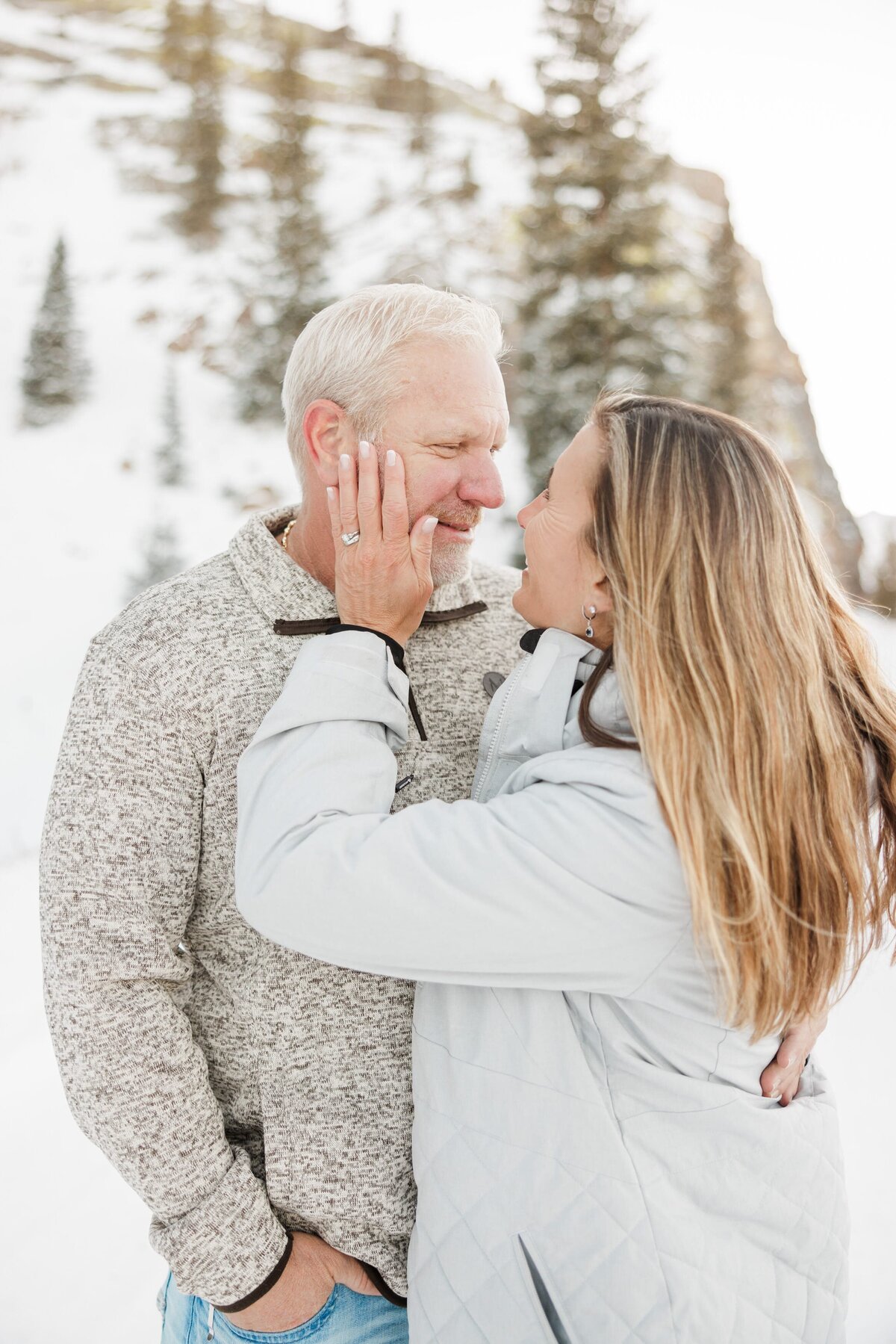 A happy woman in a white jacket leans in to kiss her husband in a snowy mountain