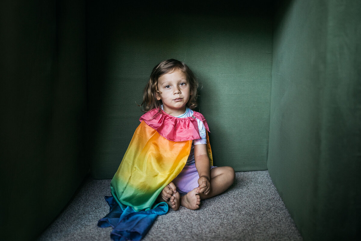 Portrait of toddler boy wearing a rainbow cape in the playroom of his home.