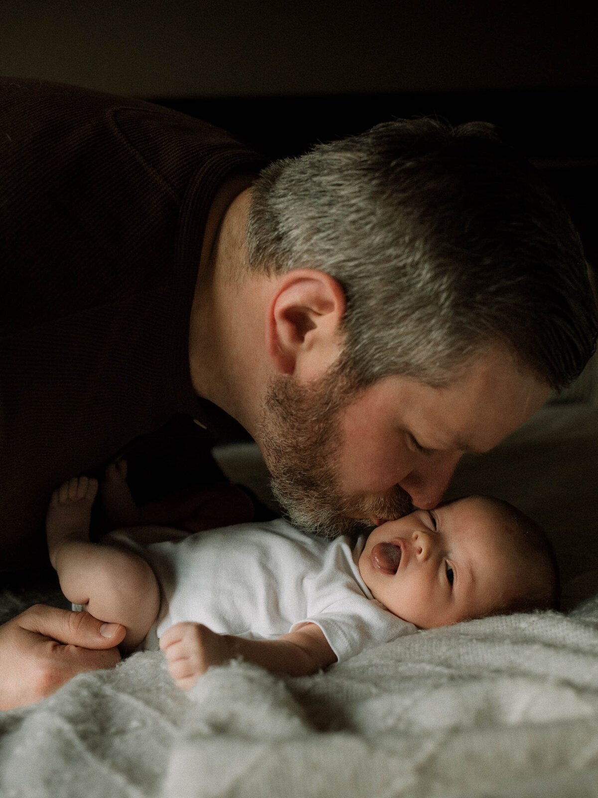 Dad gently kissing baby while laying on the bed.