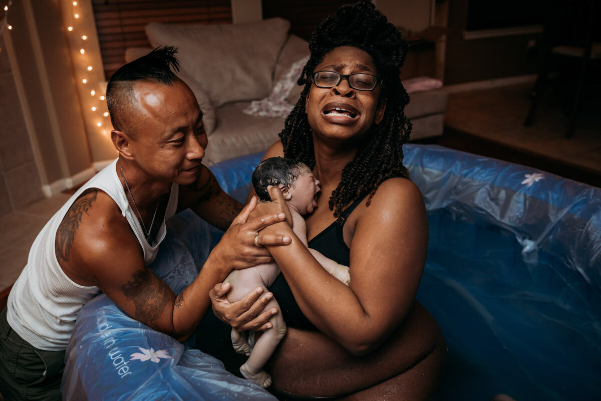 woman in birth pool crying as she holds newborn