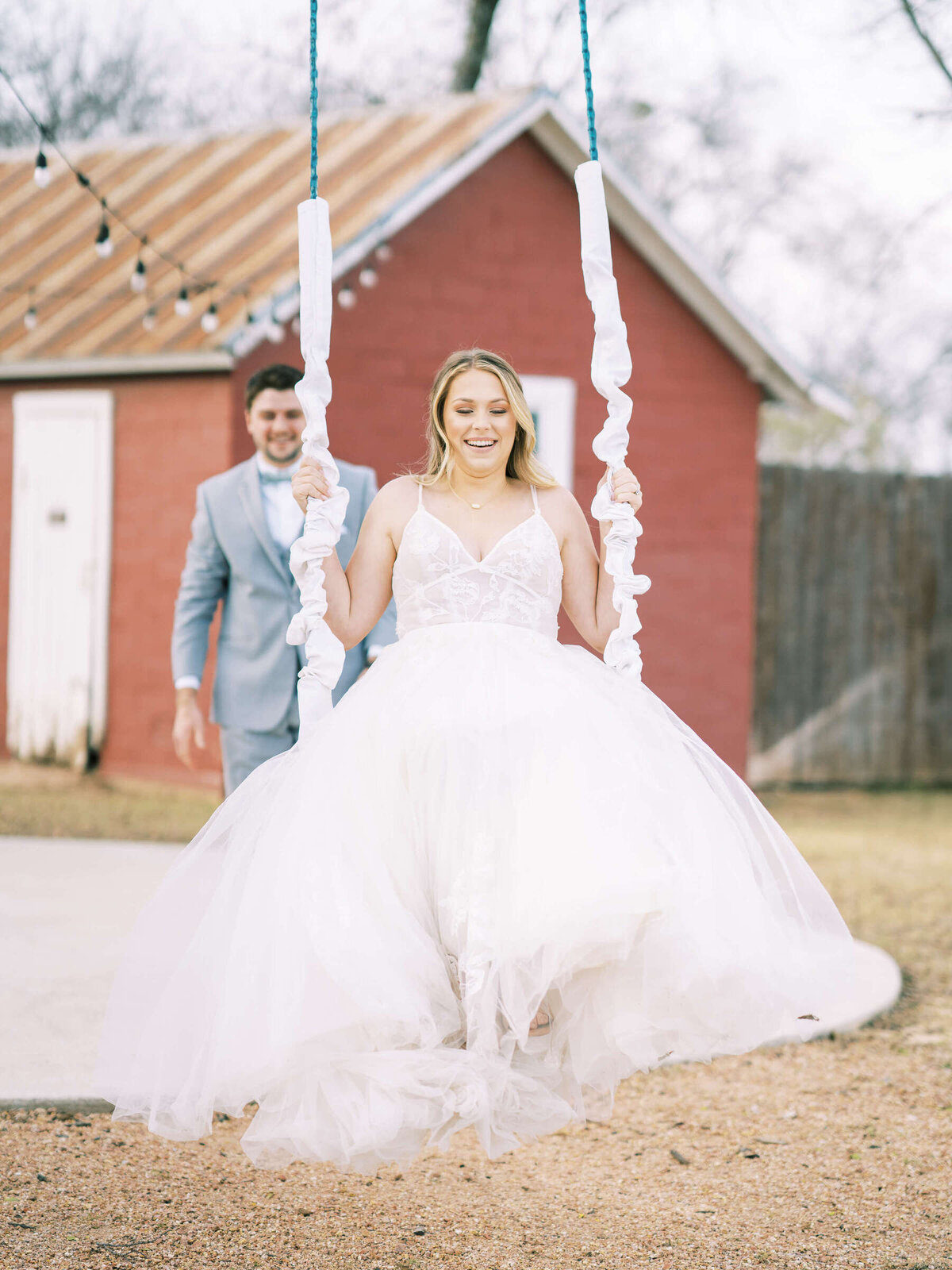 Groom pushes bride on outdoor tree swing at elegant rustic wedding in North Texas