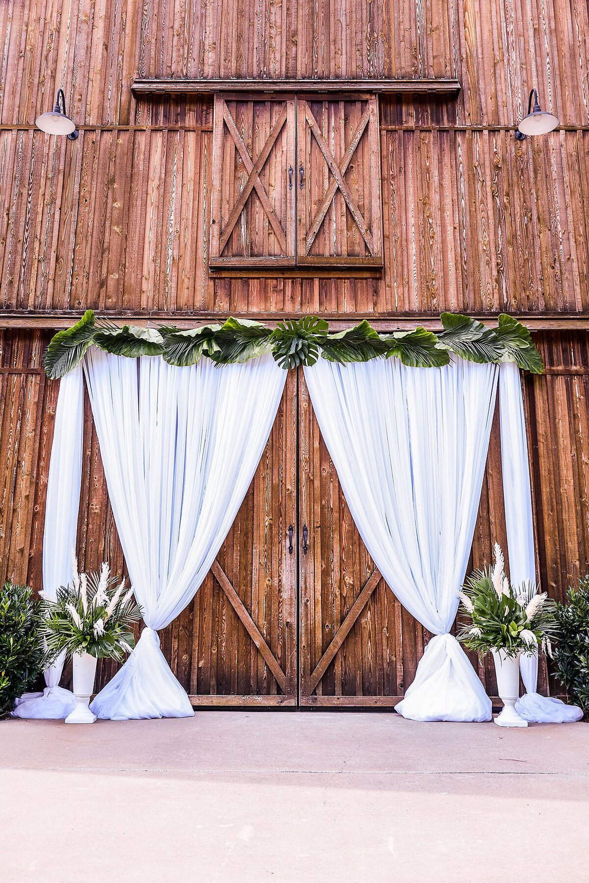 Saddlewood Farms barn doors with draping, greenery top garland, and two entrance arrangements