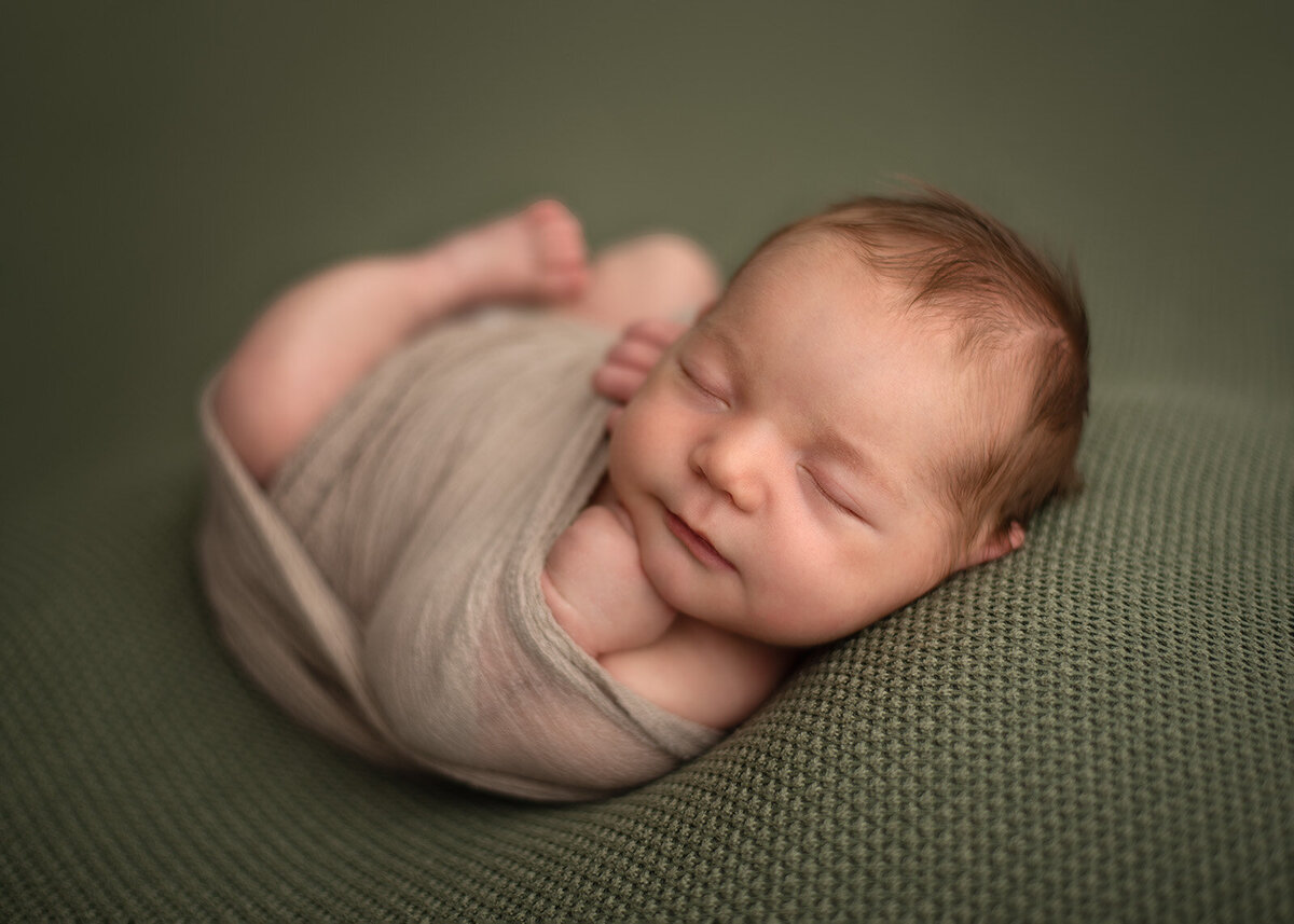 baby wrapped up with hand under chin on a green blanket by st. louis newborn photographer