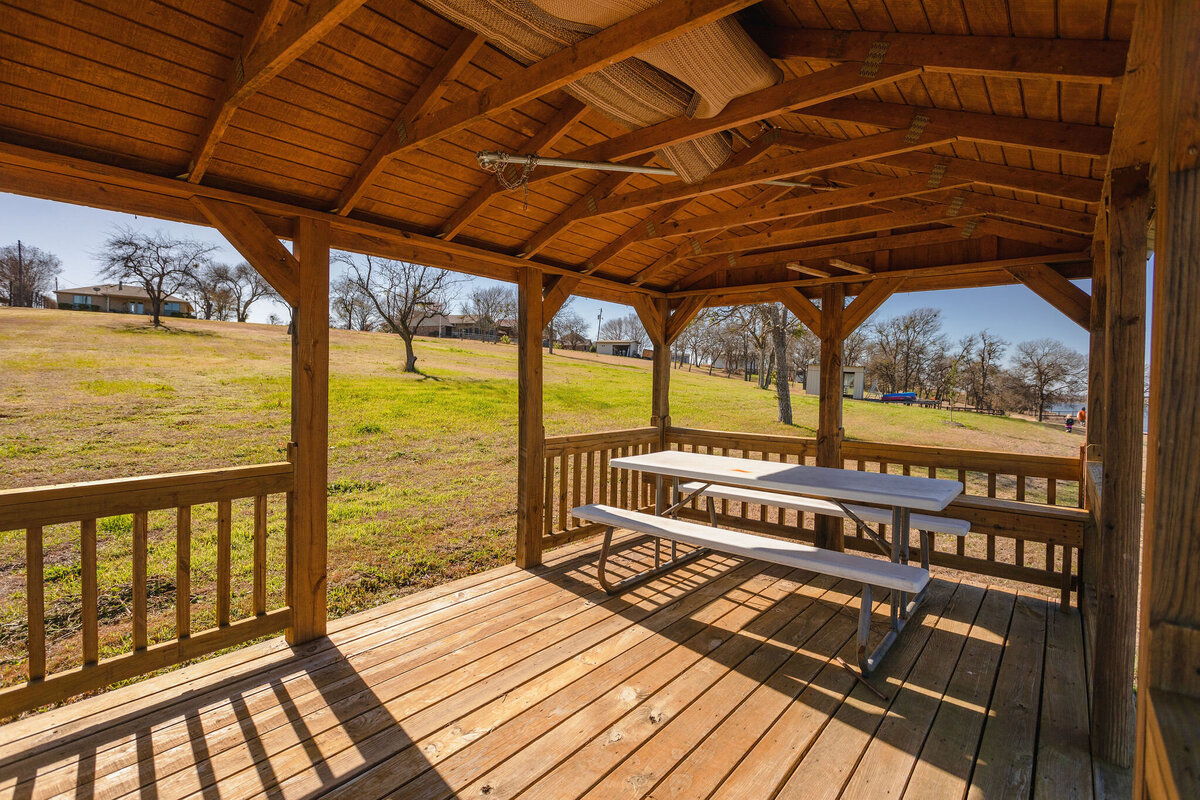 Covered outdoor patio with picnic table at this 2-bedroom, 2-bathroom lakeside vacation rental home for 6 guests on Tradinghouse Lake with privacy access to a fishing dock and boat launch pad, ping pong table, gazebo, free wifi and free parking in Waco, TX.