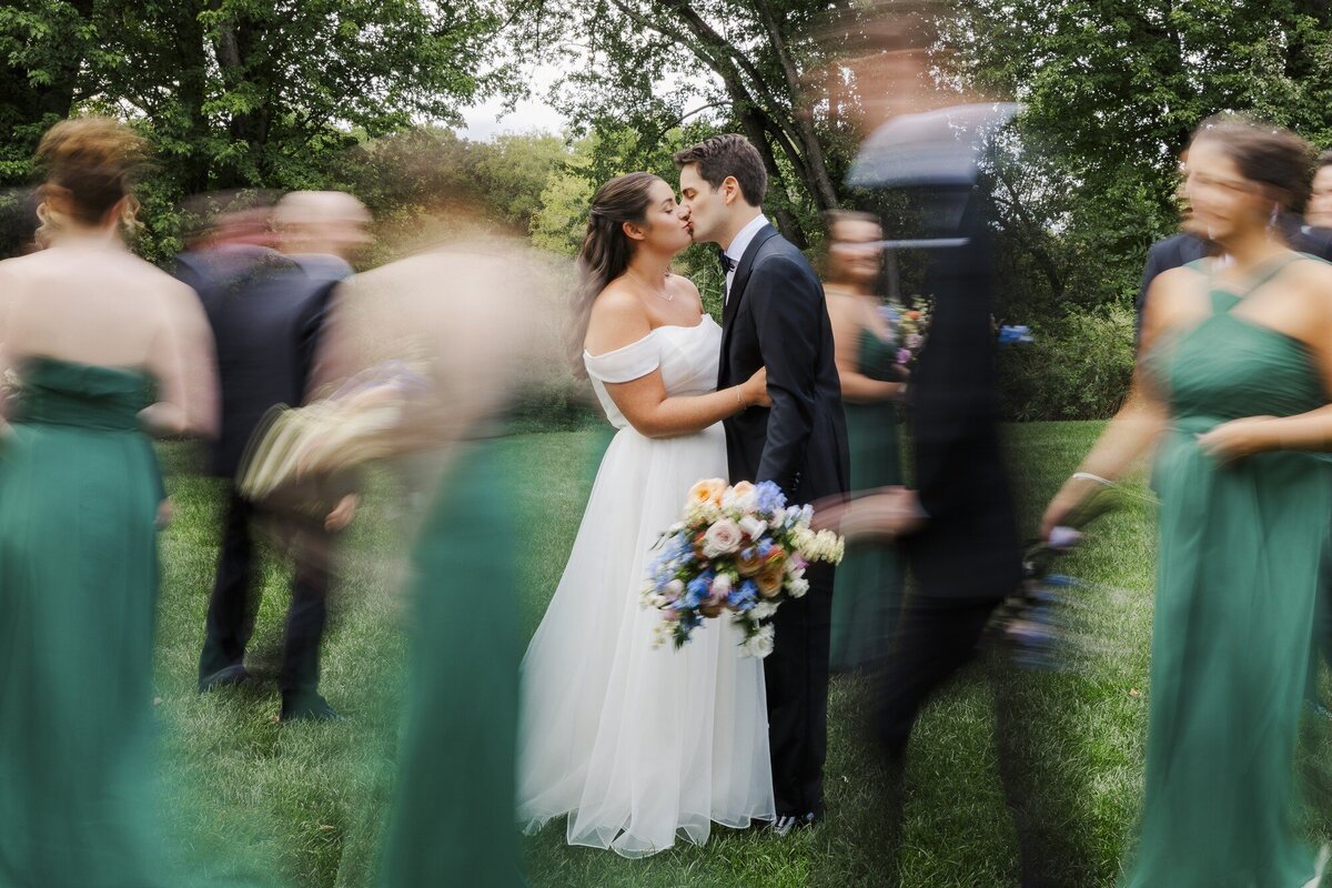 Bride and groom kiss as their wedding party rushes past in a long exposure