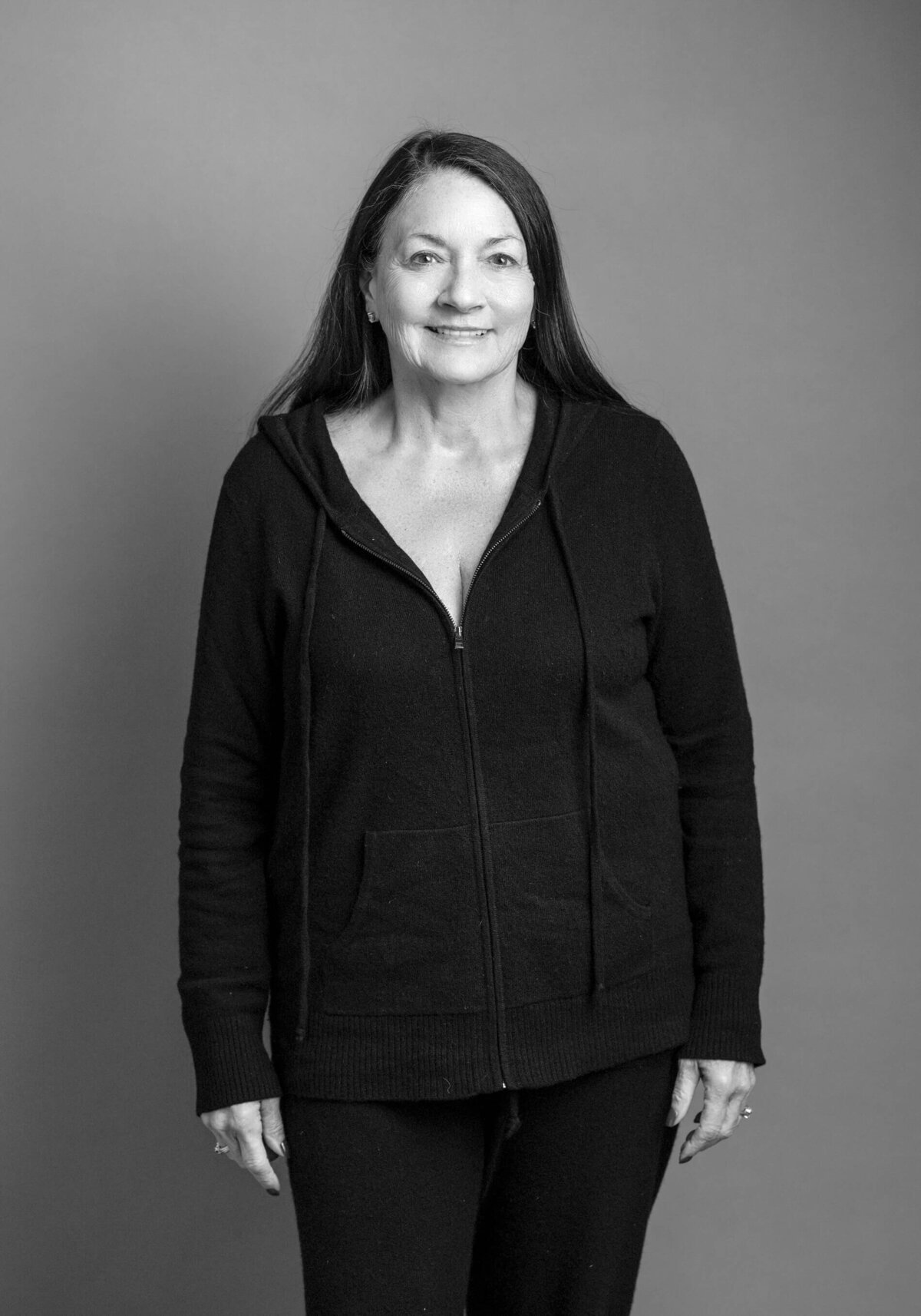 Before shot of a woman in a black hoodie, standing confidently with a warm expression.