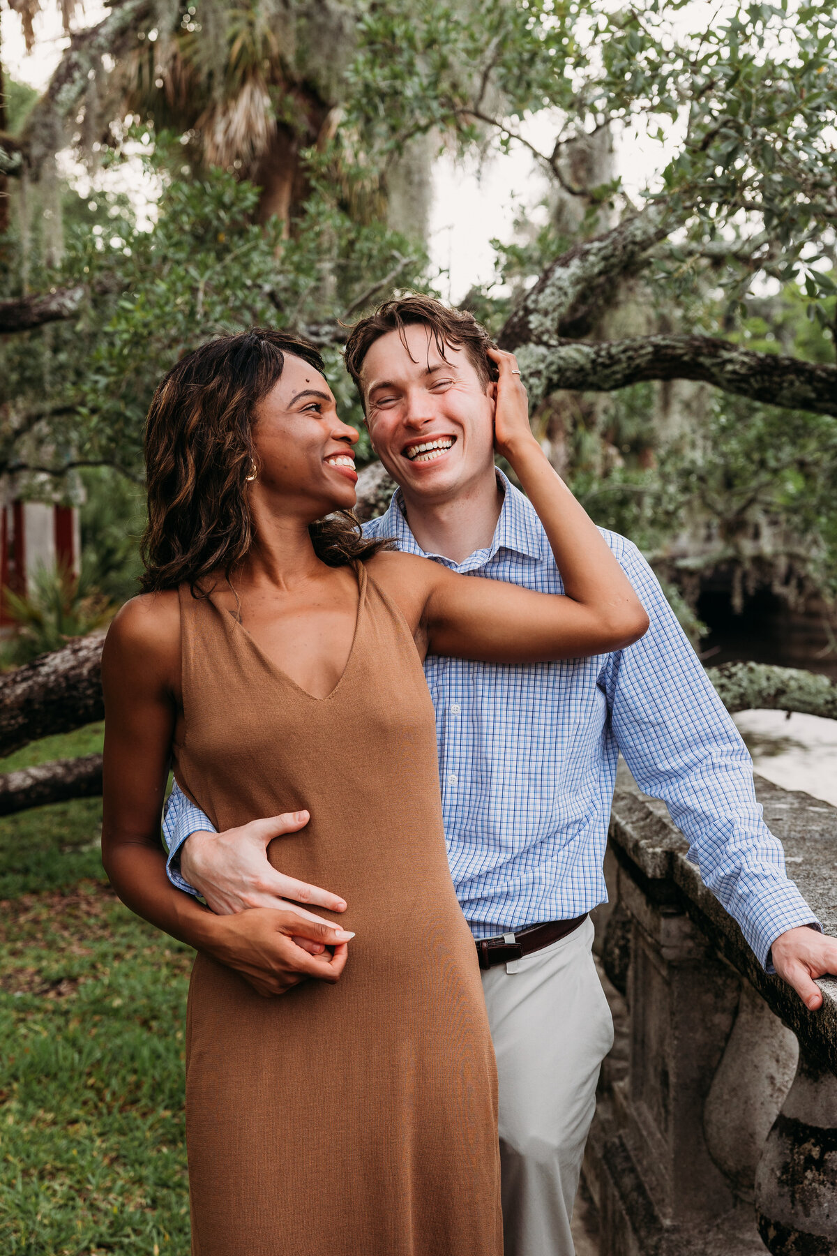 Couple embraces under moss-draped trees in Jacksonville during a romantic engagement session filled with laughter and warmth