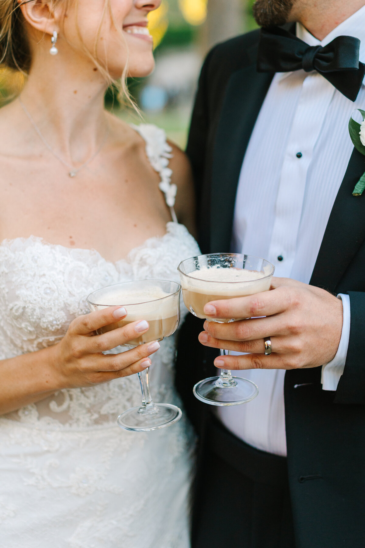 bride and groom holding coupes of champagne and smiling at each other.