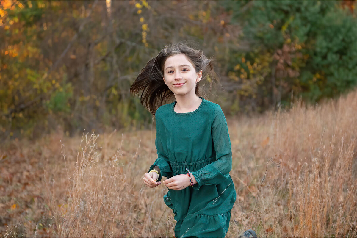 A girl in a green dress runs through a field at the Minute Man trail with her hair in the wind.