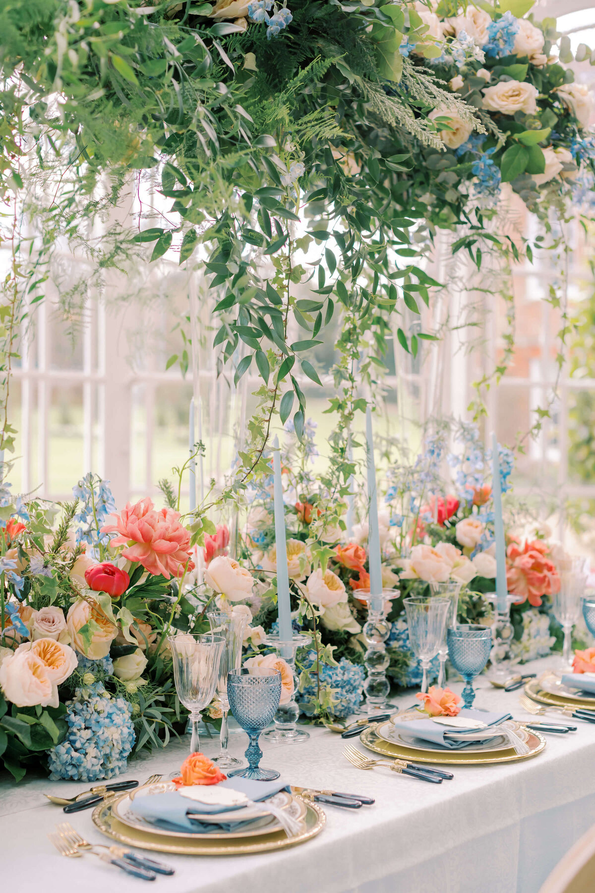 blue and coral themed wedding dinner table in the orangery glasshouse at avington park with blue and coral flowers and blue water glasses