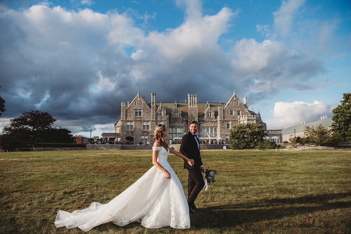 bride and groom walk in front of their branford house wedding venue in sunlight and venue in background photo by cait fletcher photography