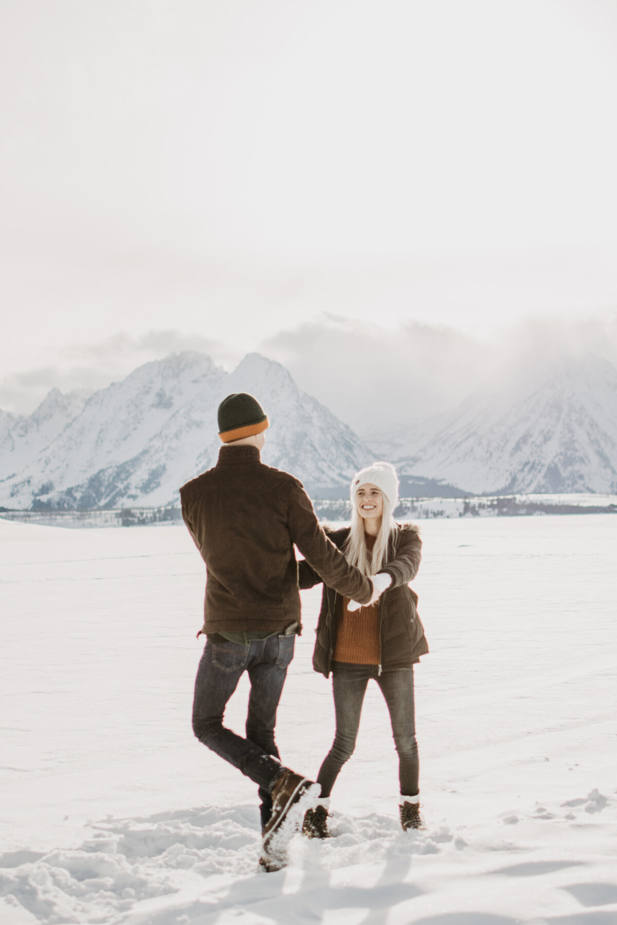 engagement session in the Tetons with man and woman dancing in the snow with the Tetons behind them