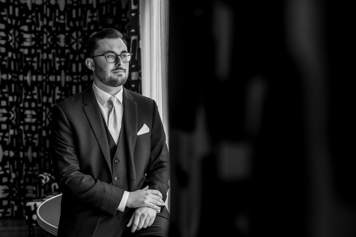 a black and white photo of a groom looking out a window