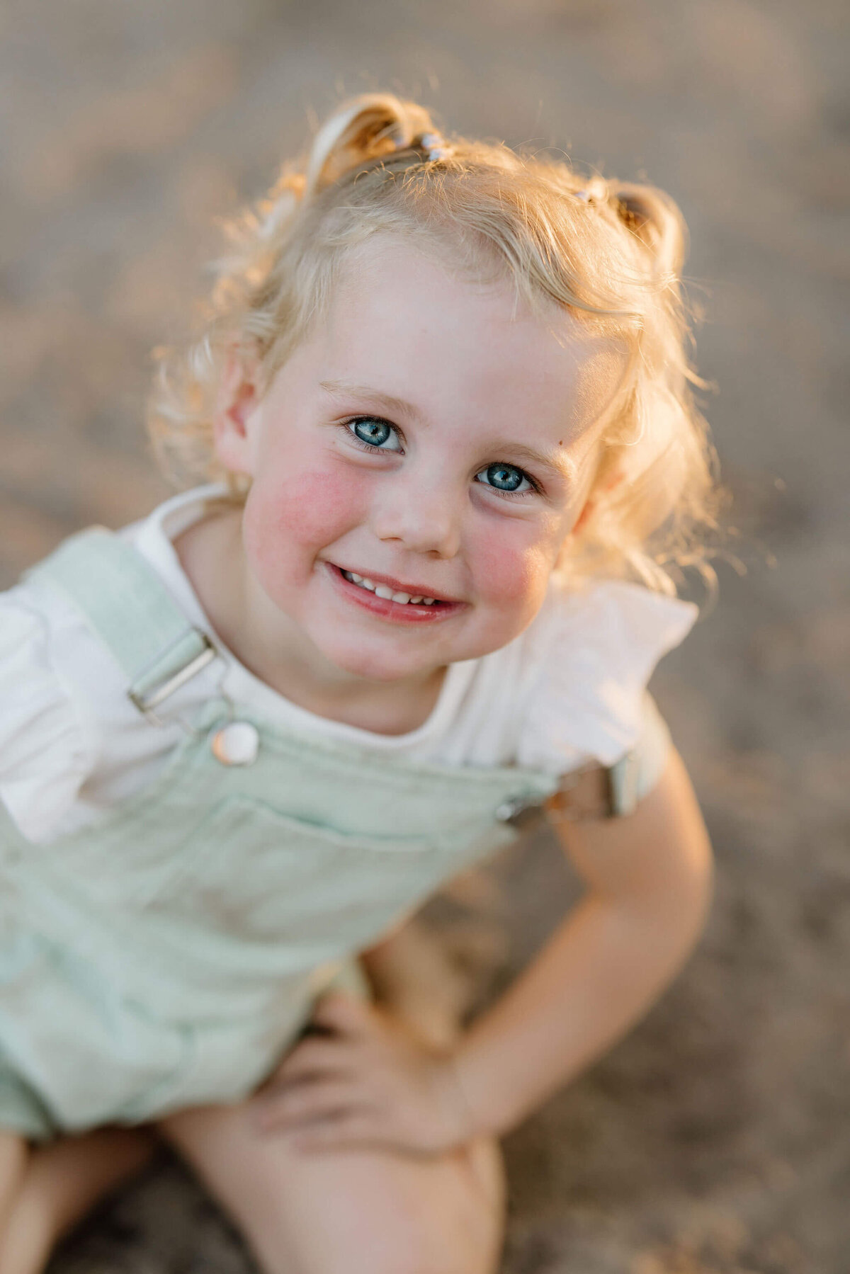 up close 3 year old birthday photo of blonde girl in green overalls