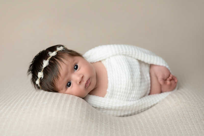 Newborn baby swaddled in white wrap lying peacefully during Houston newborn photography session.