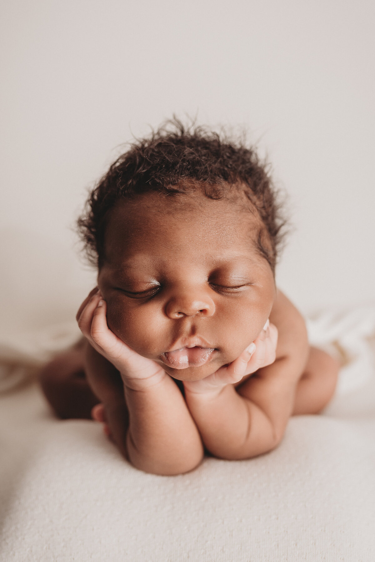 2 week old baby boy with chin on hands asleep on white cloth backdrop