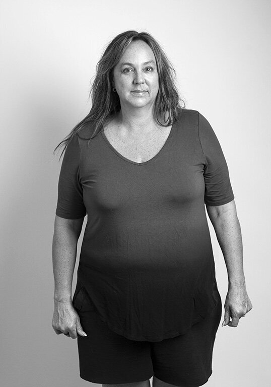 Black and white before shot of a woman with long hair, smiling with her hands at her sides.