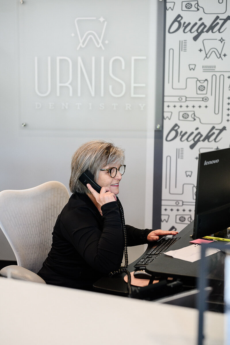 A brand photographer in Denver takes a picture of a woman answering a phone in a dental office for a denver branding photography session for branding photos and brand pictures.
