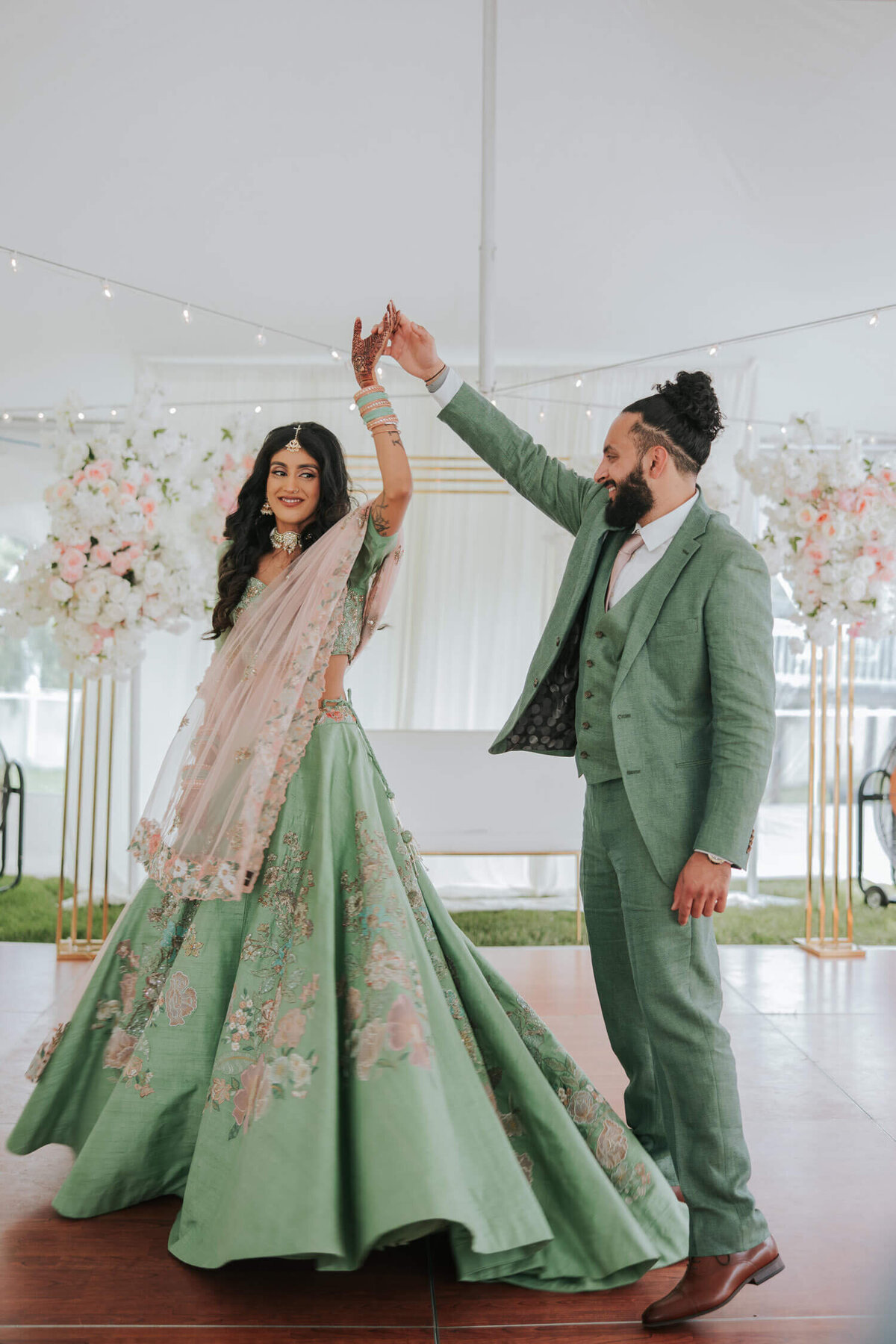 A couple shares a joyful twirl on the dance floor, surrounded by elegant floral decorations and soft lighting