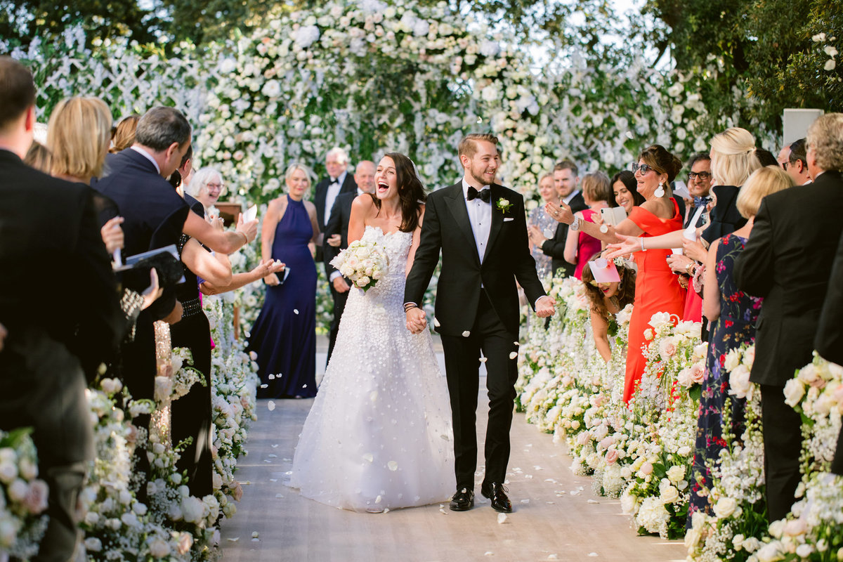 bride and groom walking down the aisle with a flower arch
