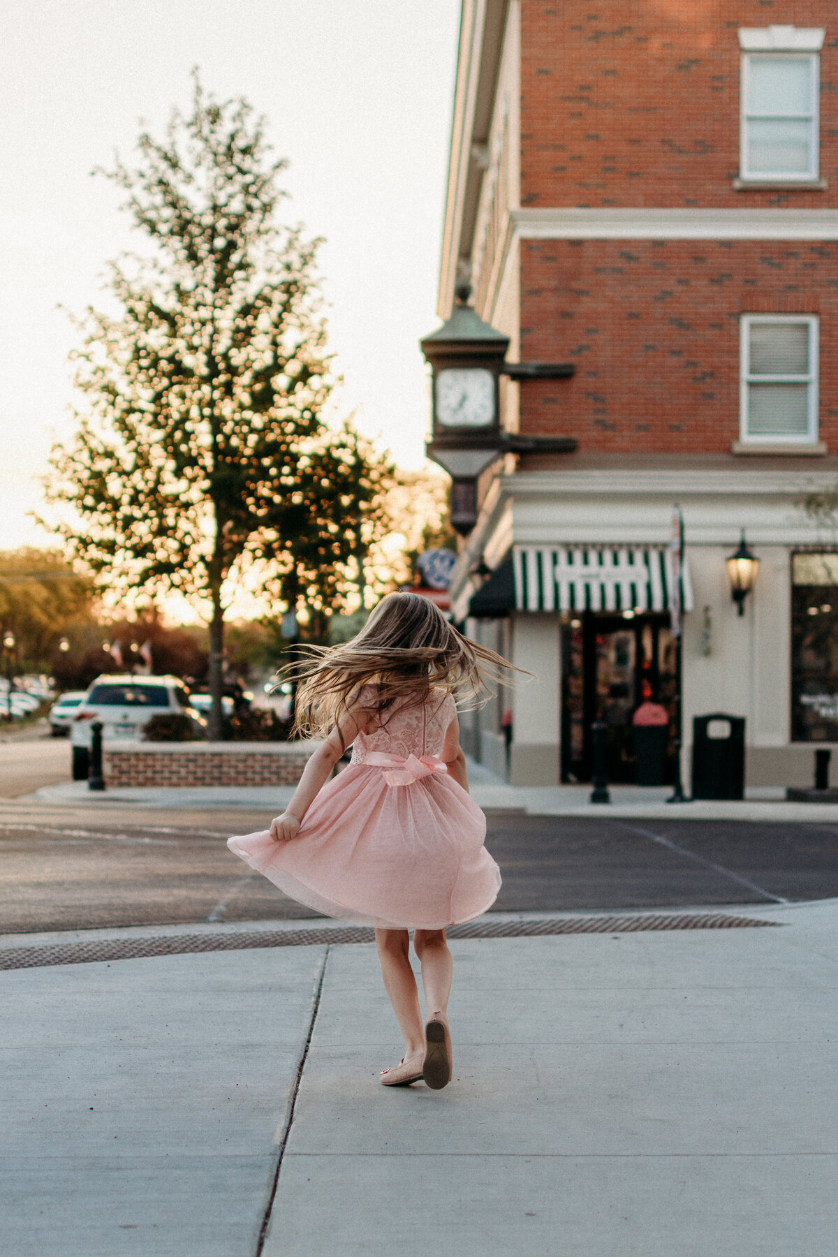 Young girl swirling in a pink dress on the streets of downtown Glen Ellyn
